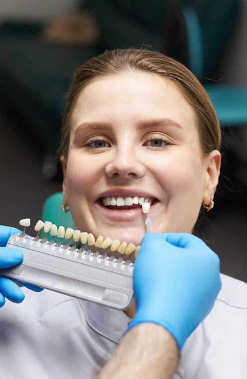 Dentist matching tooth shade for porcelain veneers on smiling female patient